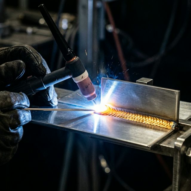 Solda TIG em aço inoxidável com arco elétrico azulado e brilho dourado.